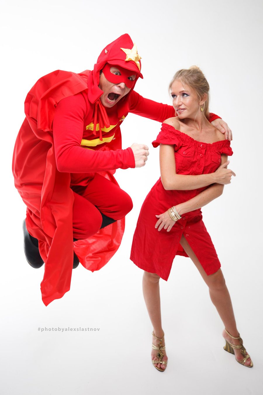 Creative studio portrait of two people in red costumes, one jumping like a superhero, on a white background