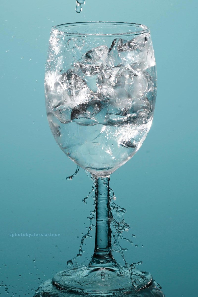 Glass photography: a wine glass with ice cubes and splashing water on a teal background