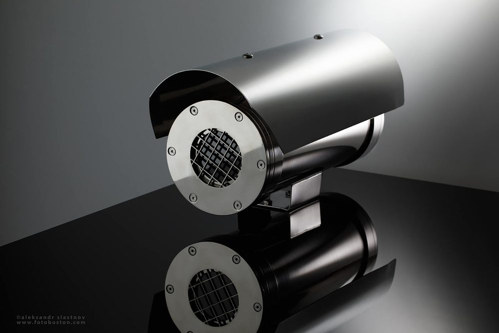 Stainless steel industrial camera housing on a reflective black surface, commercial product photography