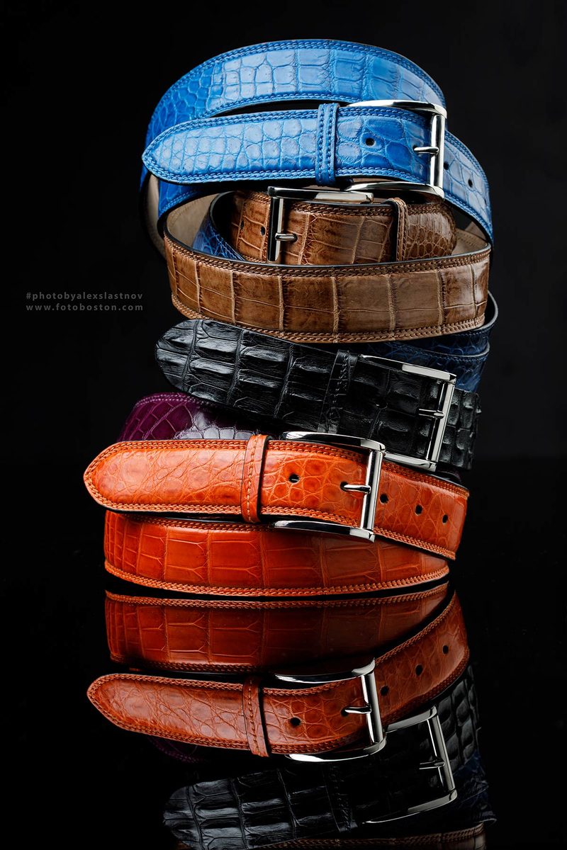 Stack of colorful crocodile-pattern leather belts with a reflection on black