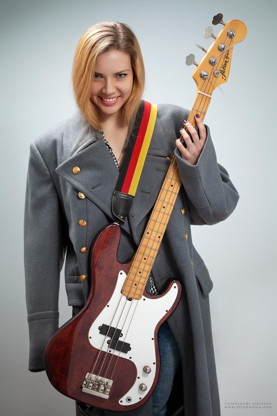 Portrait of a smiling woman in a coat holding a bass guitar in a Boston photo studio