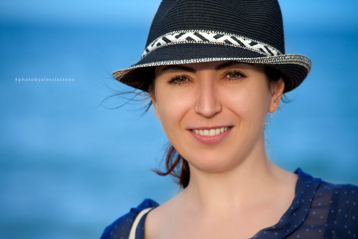 Close-up portrait of a smiling woman in a black fedora against a blue background