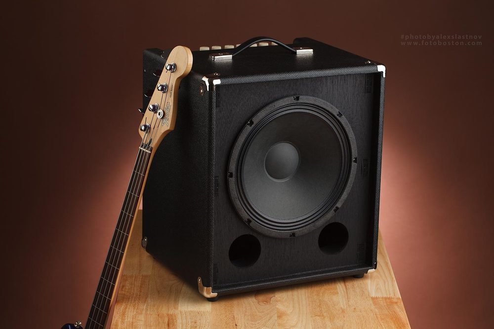 Bass amplifier cabinet with a guitar neck, lit against a warm brown backdrop