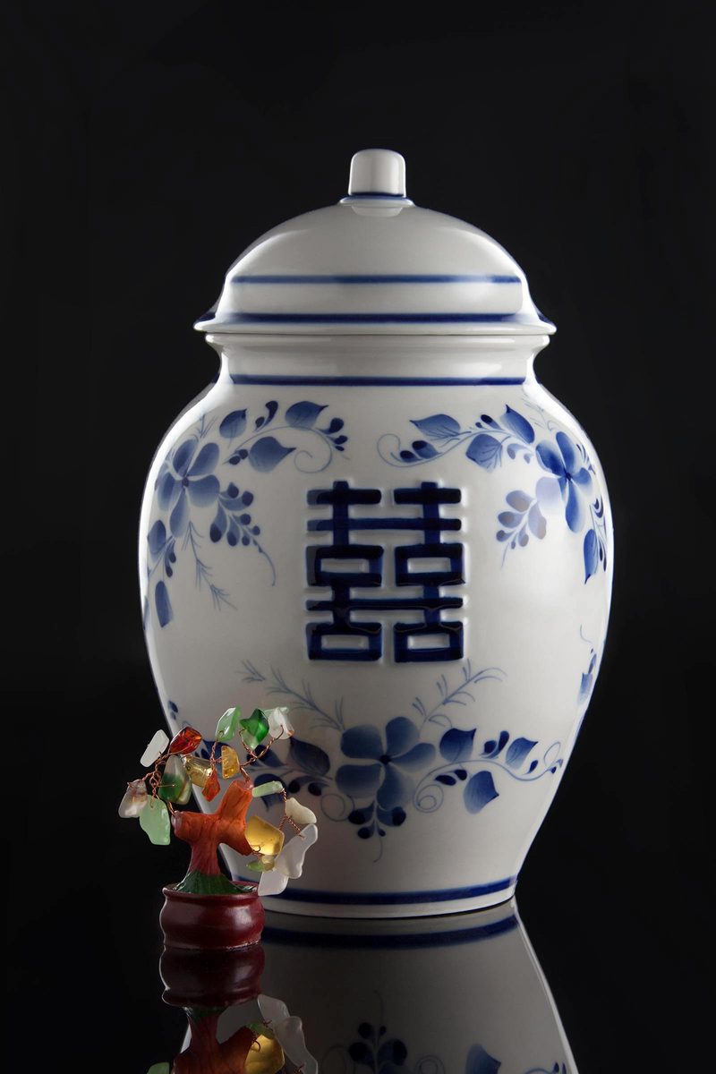 Blue and white porcelain jar with a small gemstone tree on a black reflective surface