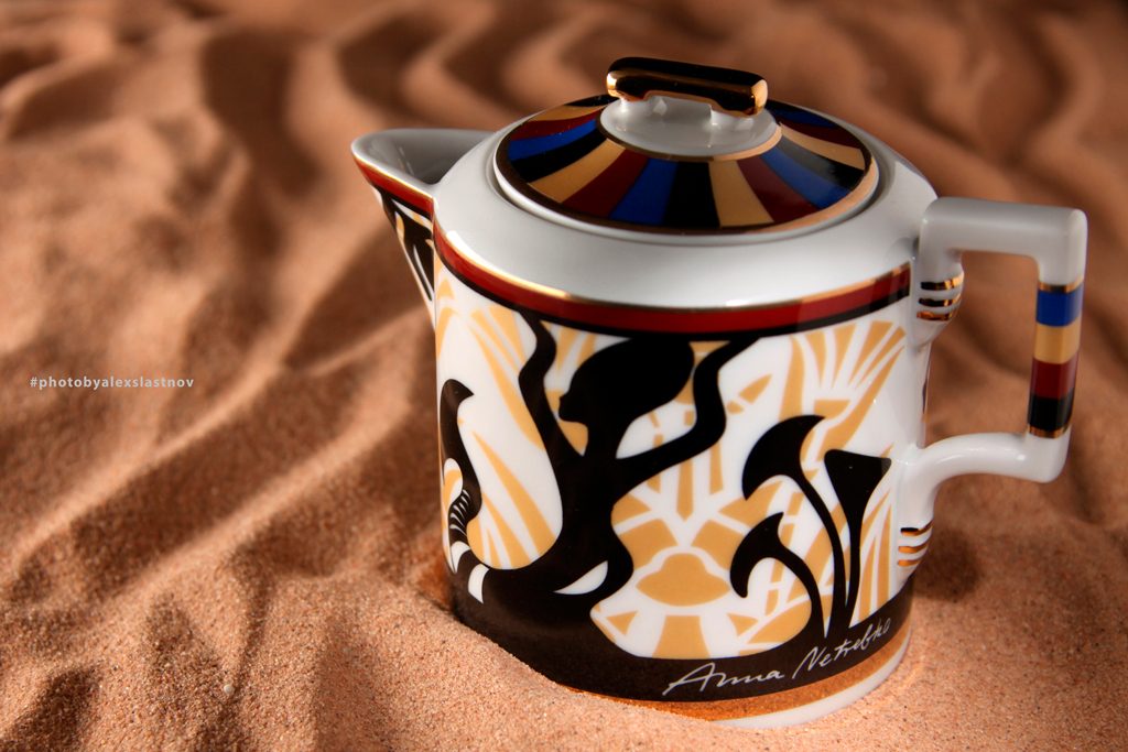 Product photo of a decorated porcelain teapot standing in rippled sand